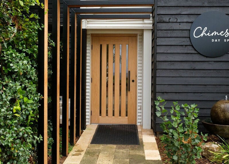 Entrance of Chimes Day Spa, featuring elegant wood door and lush greenery in Denmark, Western Australia, AU.