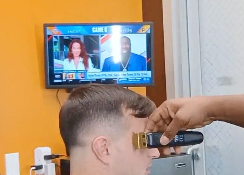 Barber giving haircut at The Introvert Men's Grooming Lounge, Chandler, Arizona, US, with TV in background.