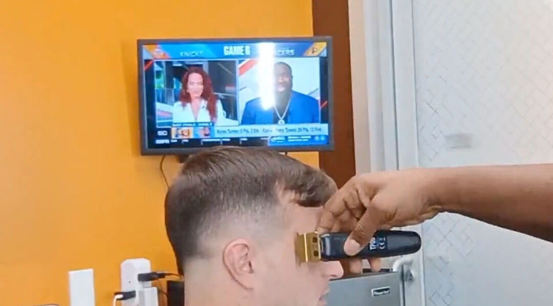 Barber giving haircut at The Introvert Men's Grooming Lounge, Chandler, Arizona, US, with TV in background.