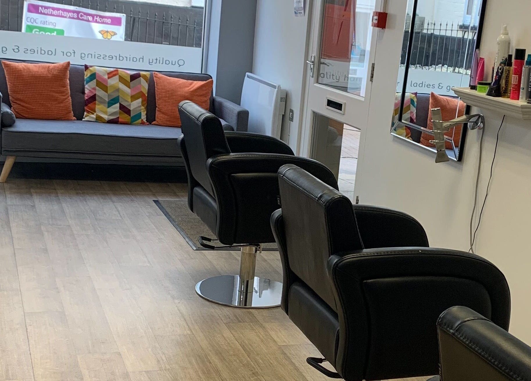 Modern salon interior at Hair at 12b in Seaton, England, GB with black chairs and cozy seating area.