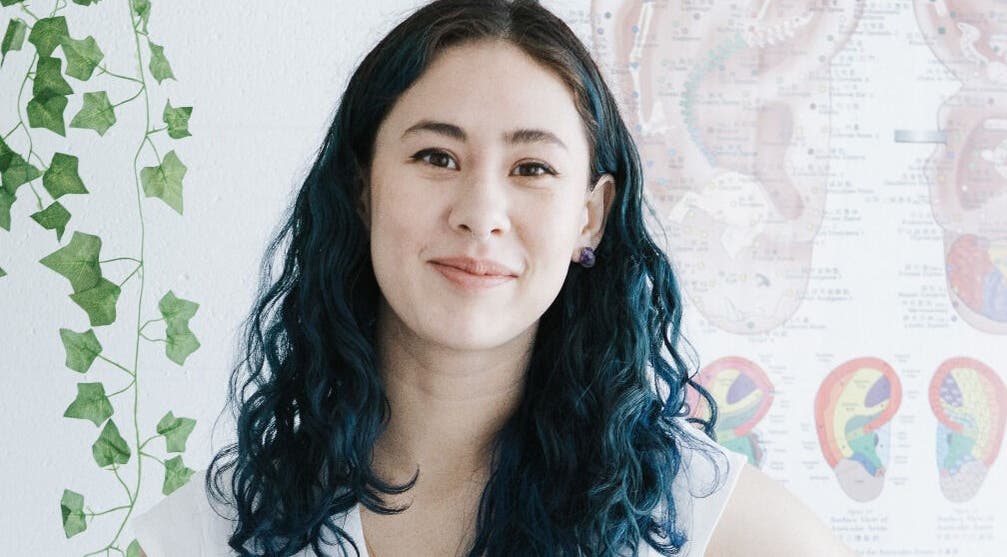 Smiling therapist at Alyssa Acupuncture & TCM, Edmonton, Alberta, CA, surrounded by educational charts.