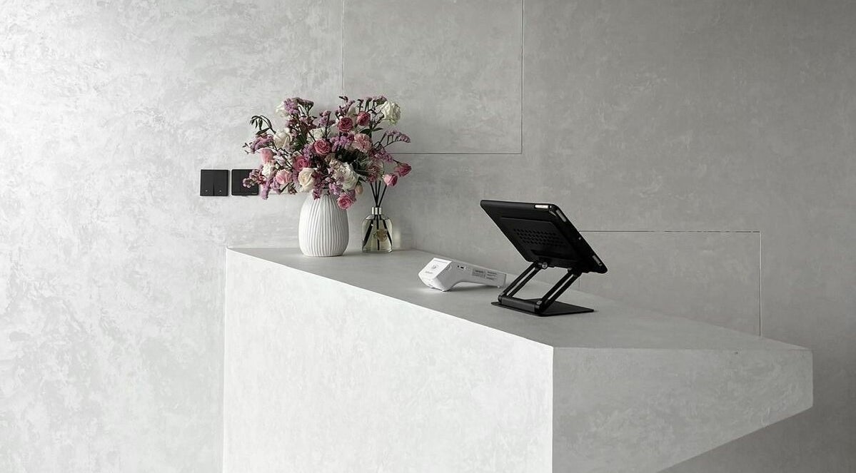 Kev Lounge Barber's sleek concrete reception in Umm Al Quwain, AE, adorned with floral decor and modern tech.