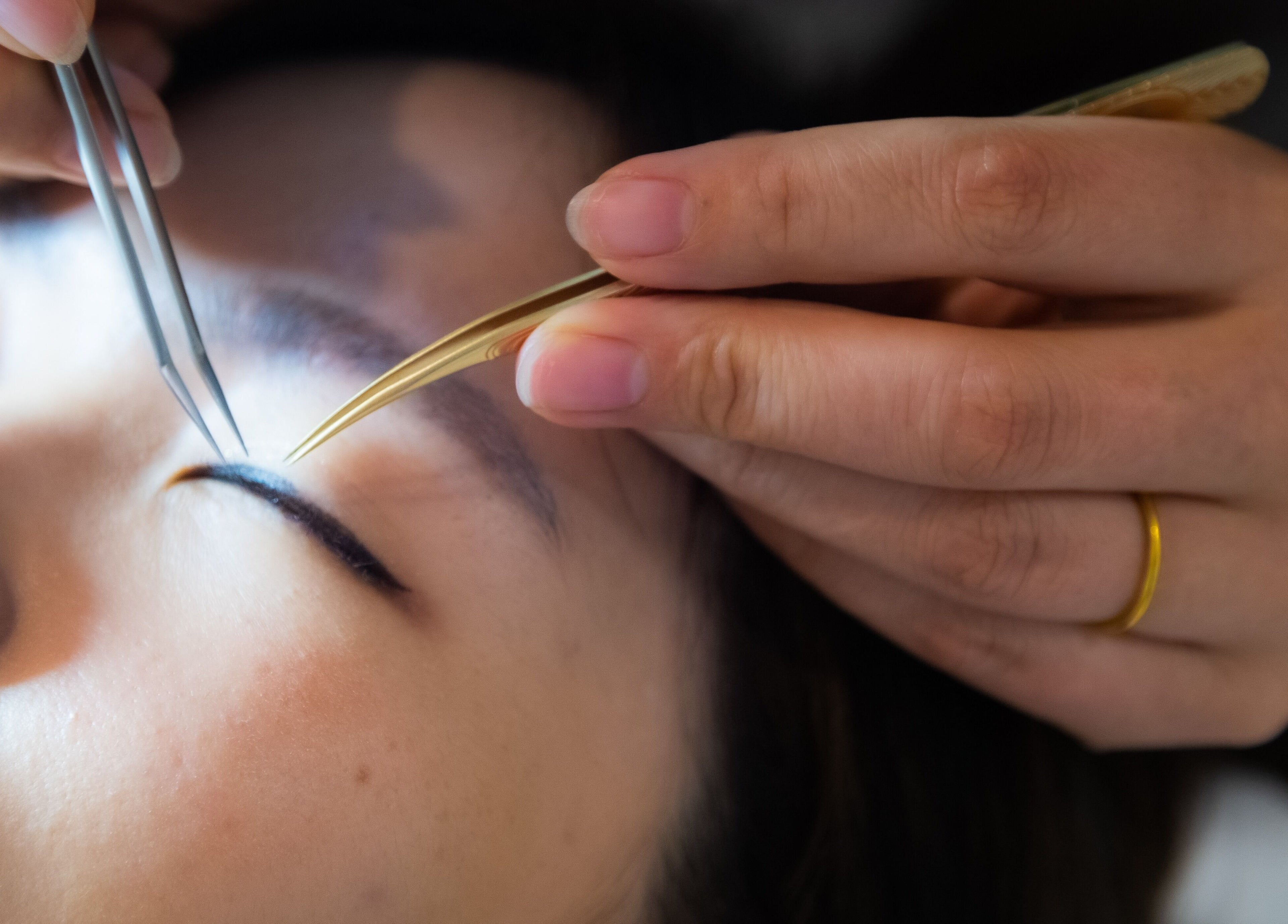 Eyelash application at Lush & Glow, Singapore, Singapore, SG. Close-up of tweezers placing an eyelash.