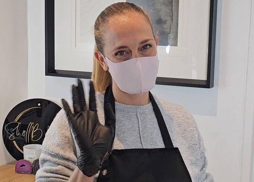 Staff member at ShellB Nails, Cape Town, Western Cape, ZA, greets with a warm gesture while wearing a mask and gloves.