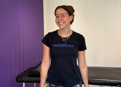 Therapist at Caitlin May Massage, Lichfield, England, GB, beside a massage table against a purple wall.