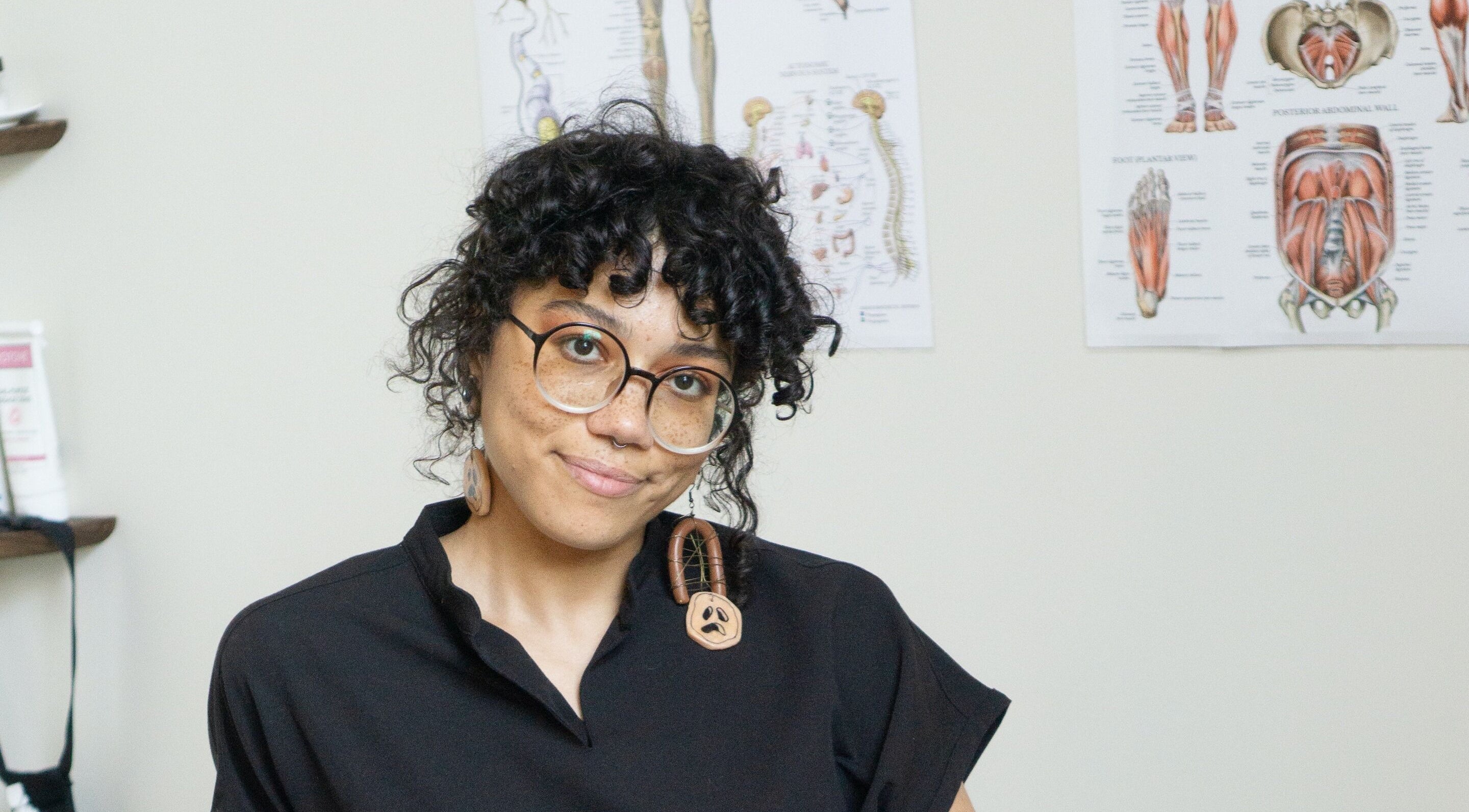 Jaz Frazier, LMT at Good Moon Bodywork in Buffalo, New York, US, amidst anatomy charts in her wellness space.
