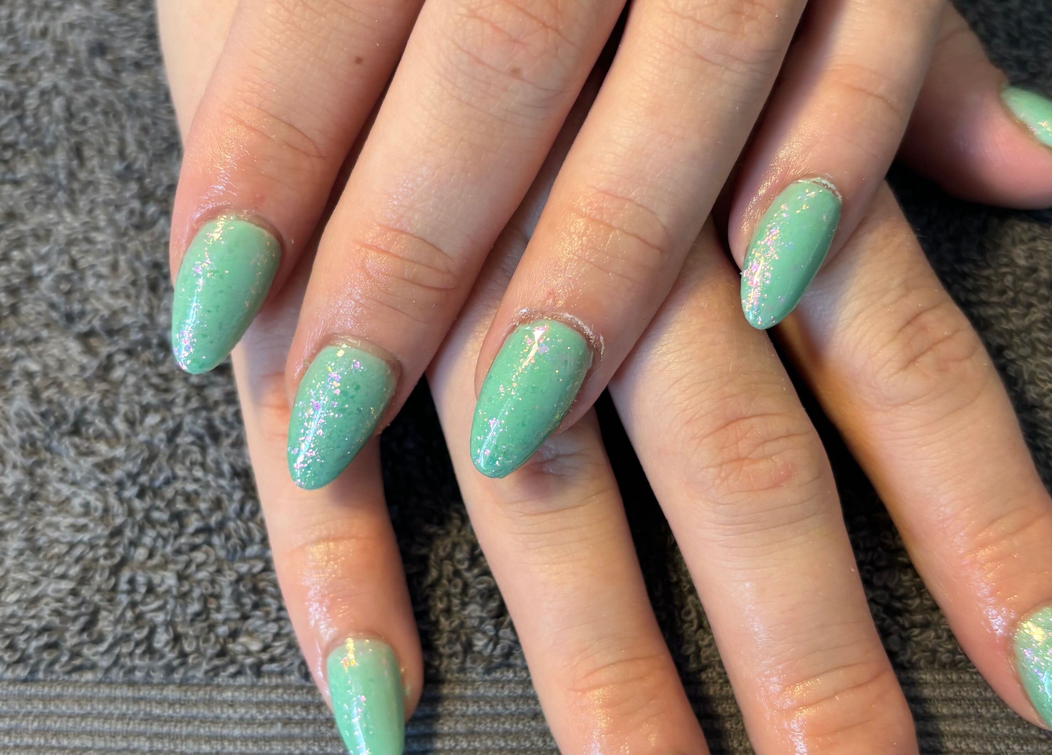 Mint green glitter nails artfully done at Nailsbyebonyy in Rainham, England, GB on a soft towel.