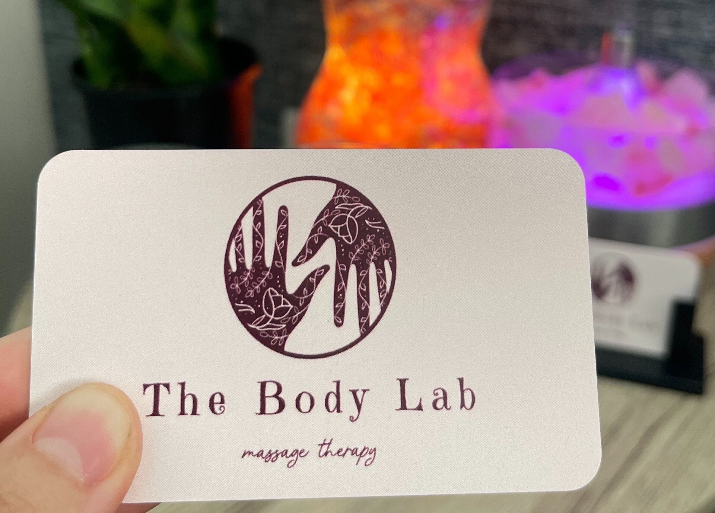The Body Lab logo on a card held in hand, Richmond, Tasman Region, NZ. Warm tones in the background enhance relaxation.