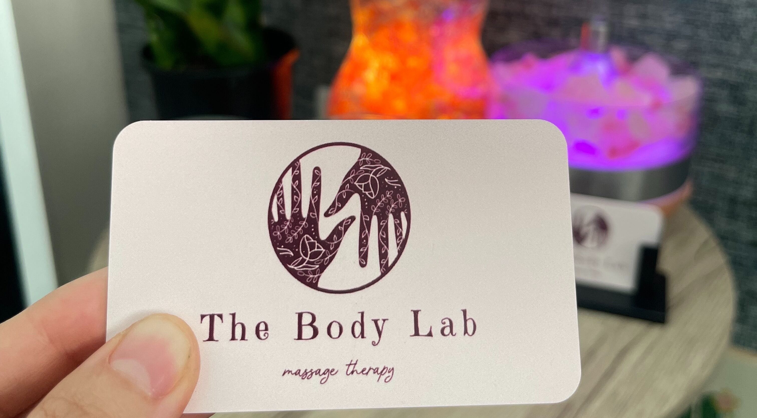 The Body Lab logo on a card held in hand, Richmond, Tasman Region, NZ. Warm tones in the background enhance relaxation.