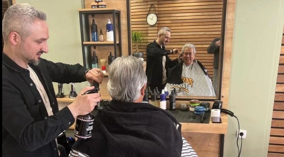 Kapper bij BarberHouse in Ede, Gelderland, NL verzorgt klant met glimlach tijdens knipbeurt.