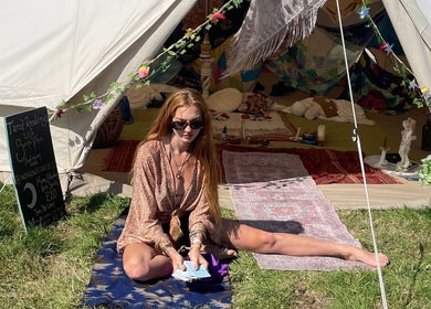 Tarot reader in front of a decorated tent at Indigo Wellness, Falmouth, England, GB, offering mystical readings.
