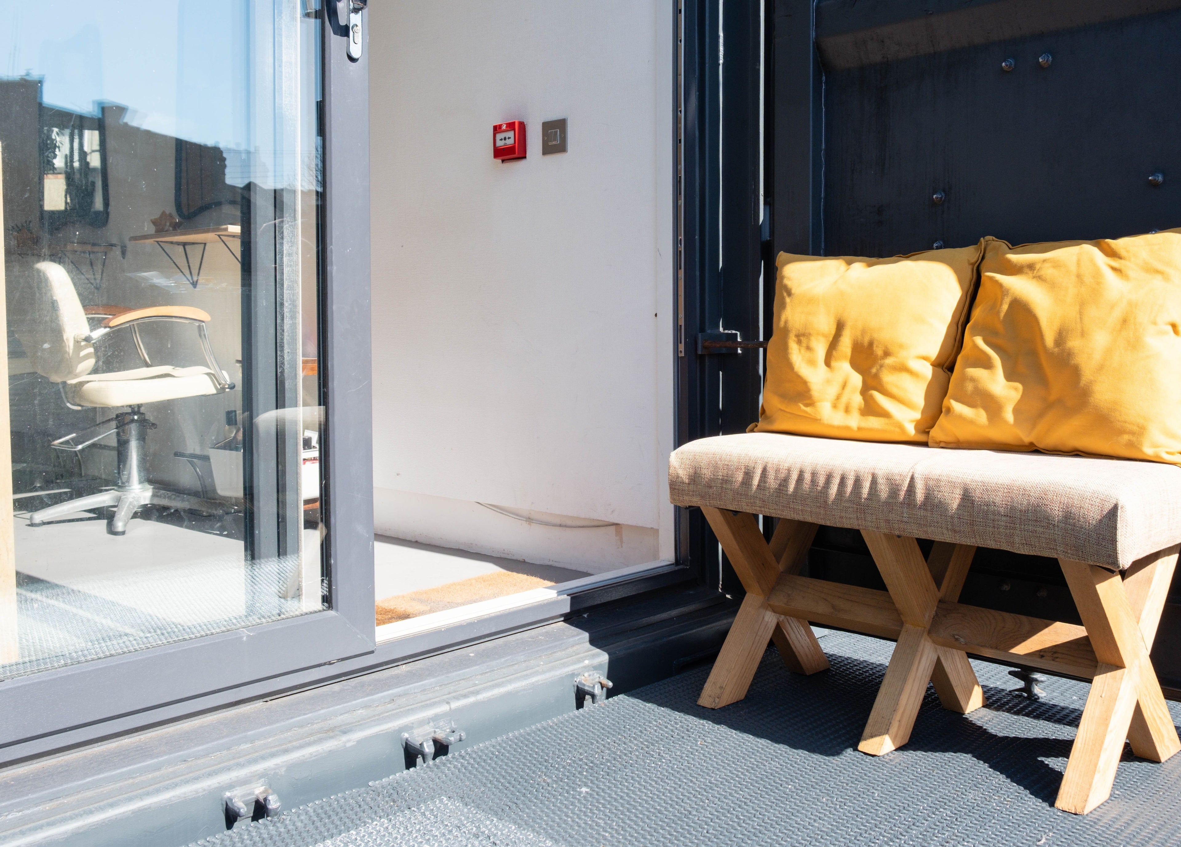 Inviting bench on Klip London's terrace, London, England, GB, with bright cushions beside a glass door.