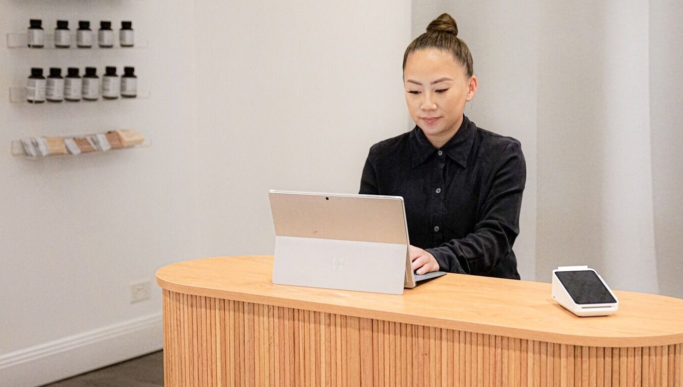 Receptionist at Blanc to Noir, Canley Heights, New South Wales, AU using a laptop at a modern wooden counter.