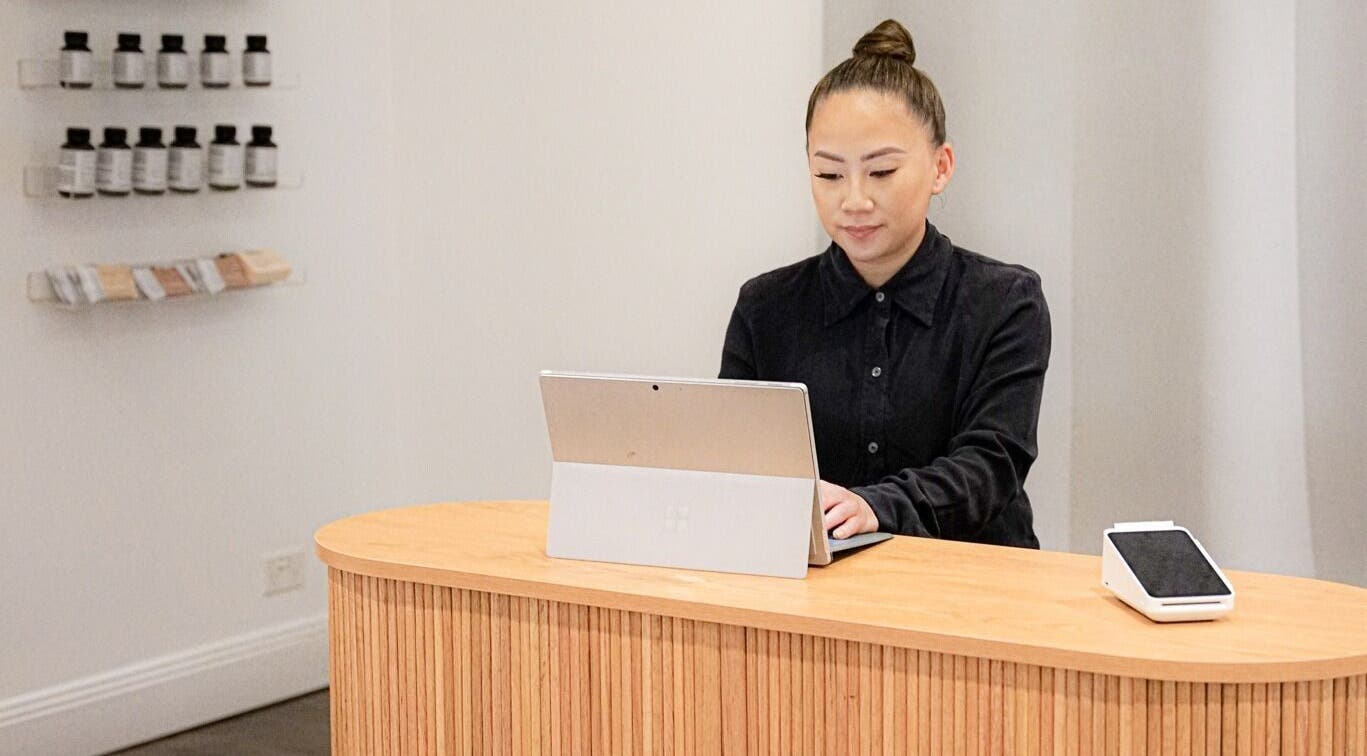 Receptionist at Blanc to Noir, Canley Heights, New South Wales, AU using a laptop at a modern wooden counter.