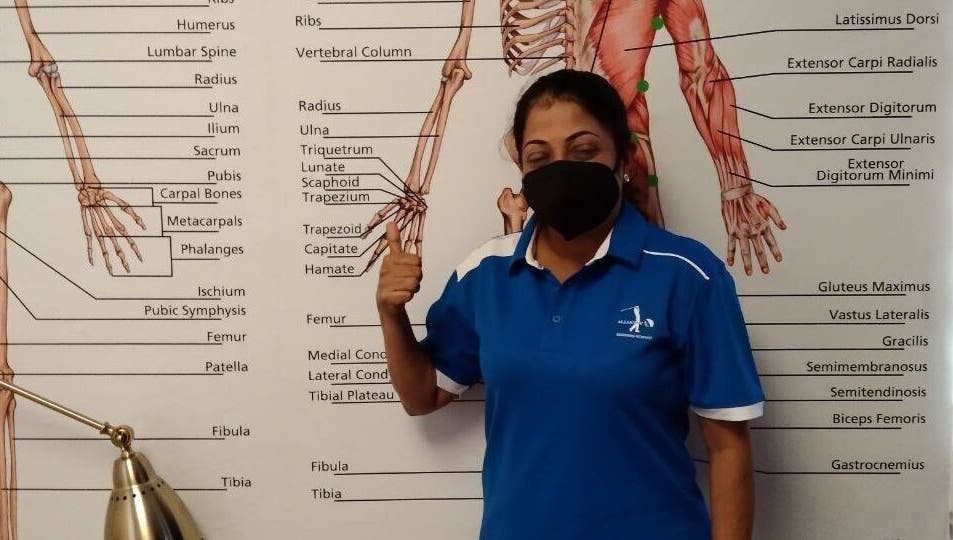 Instructor at Advanced Muscle Therapy in Petaling Jaya, Selangor, MY, standing by anatomy chart.