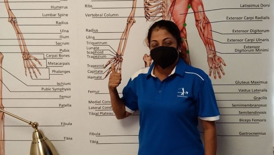 Instructor at Advanced Muscle Therapy in Petaling Jaya, Selangor, MY, standing by anatomy chart.