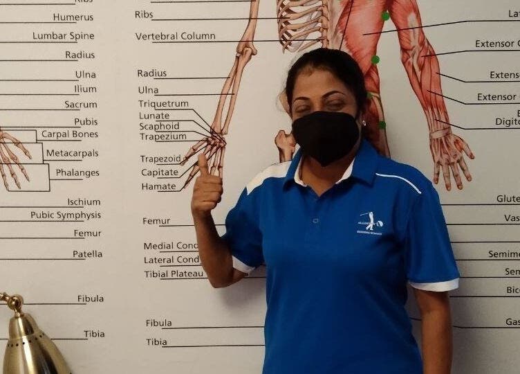 Instructor at Advanced Muscle Therapy in Petaling Jaya, Selangor, MY, standing by anatomy chart.