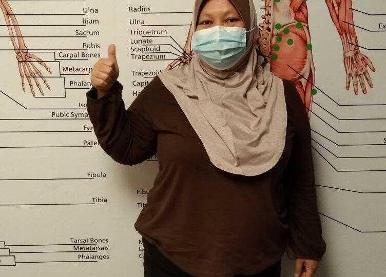 Staff at Advanced Muscle Therapy, Petaling Jaya, Selangor, MY, in front of anatomical chart, wearing a mask.