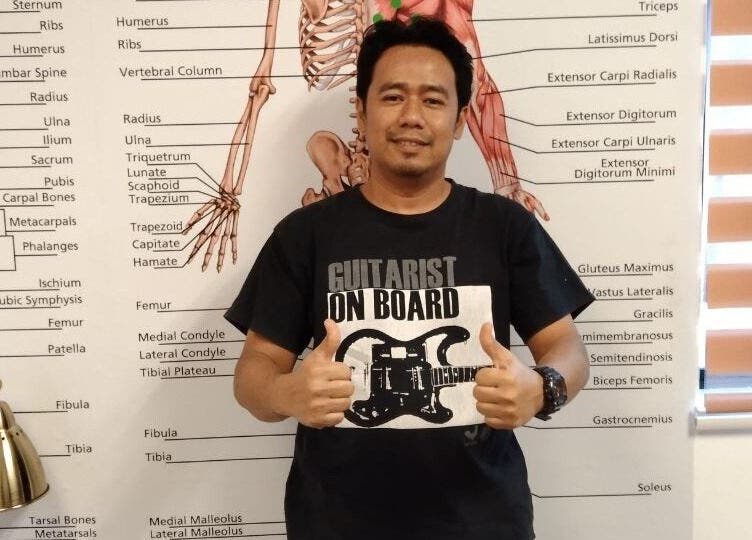 Therapist at Advanced Muscle Therapy, Petaling Jaya, Selangor, MY, poses before an anatomy chart.