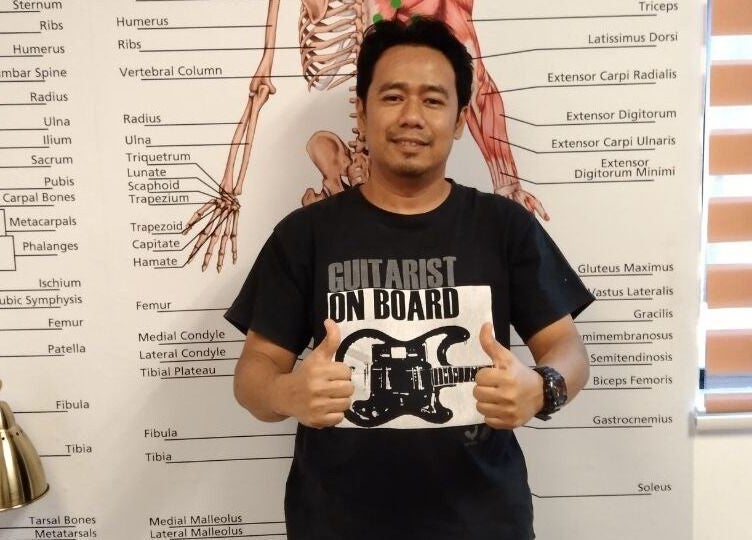 Therapist at Advanced Muscle Therapy, Petaling Jaya, Selangor, MY, poses before an anatomy chart.