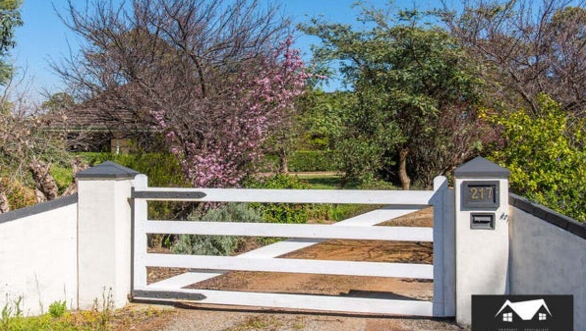 White gate entrance surrounded by lush greenery at Oh Tan, Mundijong, Western Australia, AU.