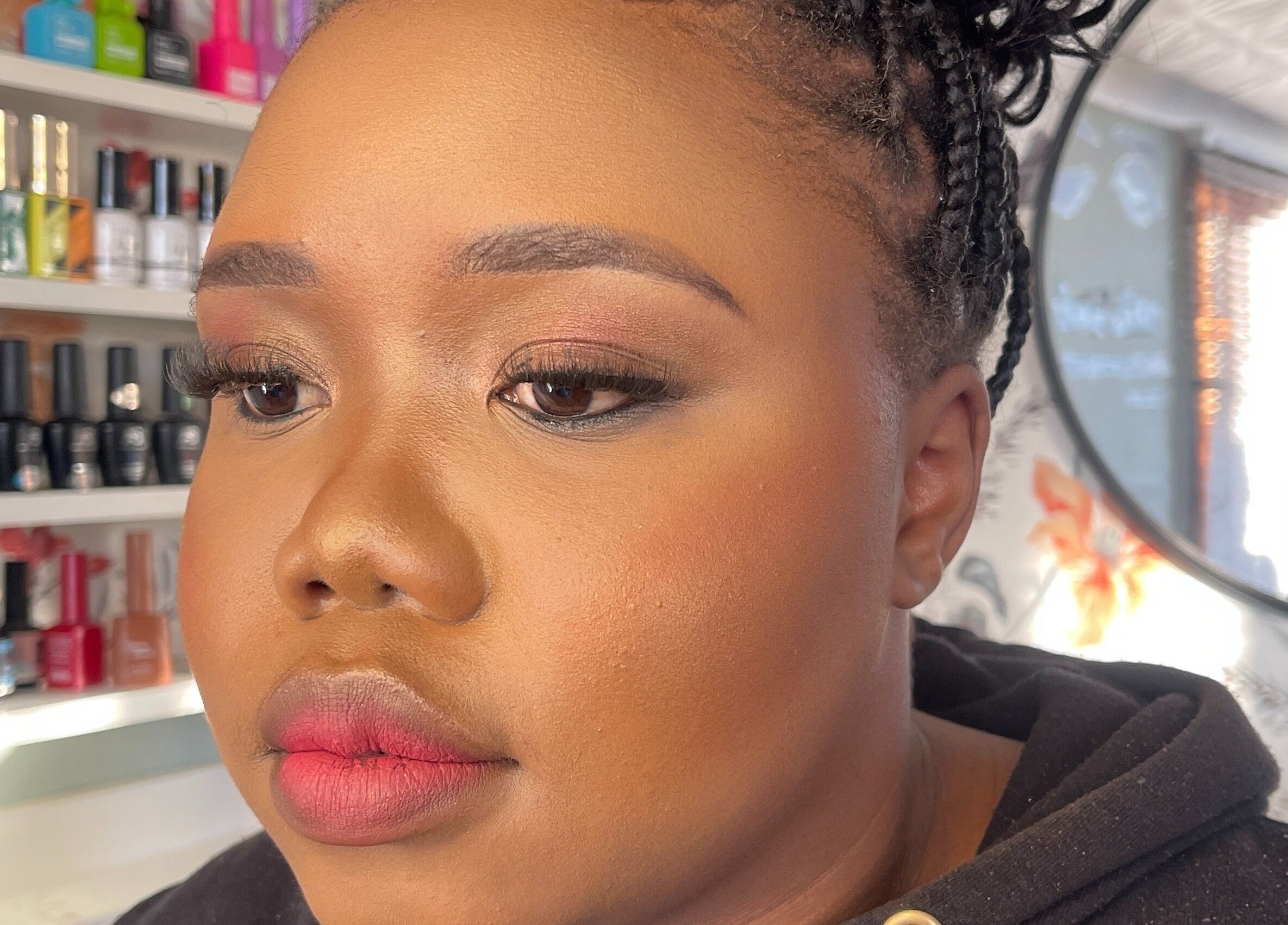 Close-up of a woman with makeup at African Girls Hair, Roodepoort, Gauteng, ZA. Shelves with nail polish are visible.