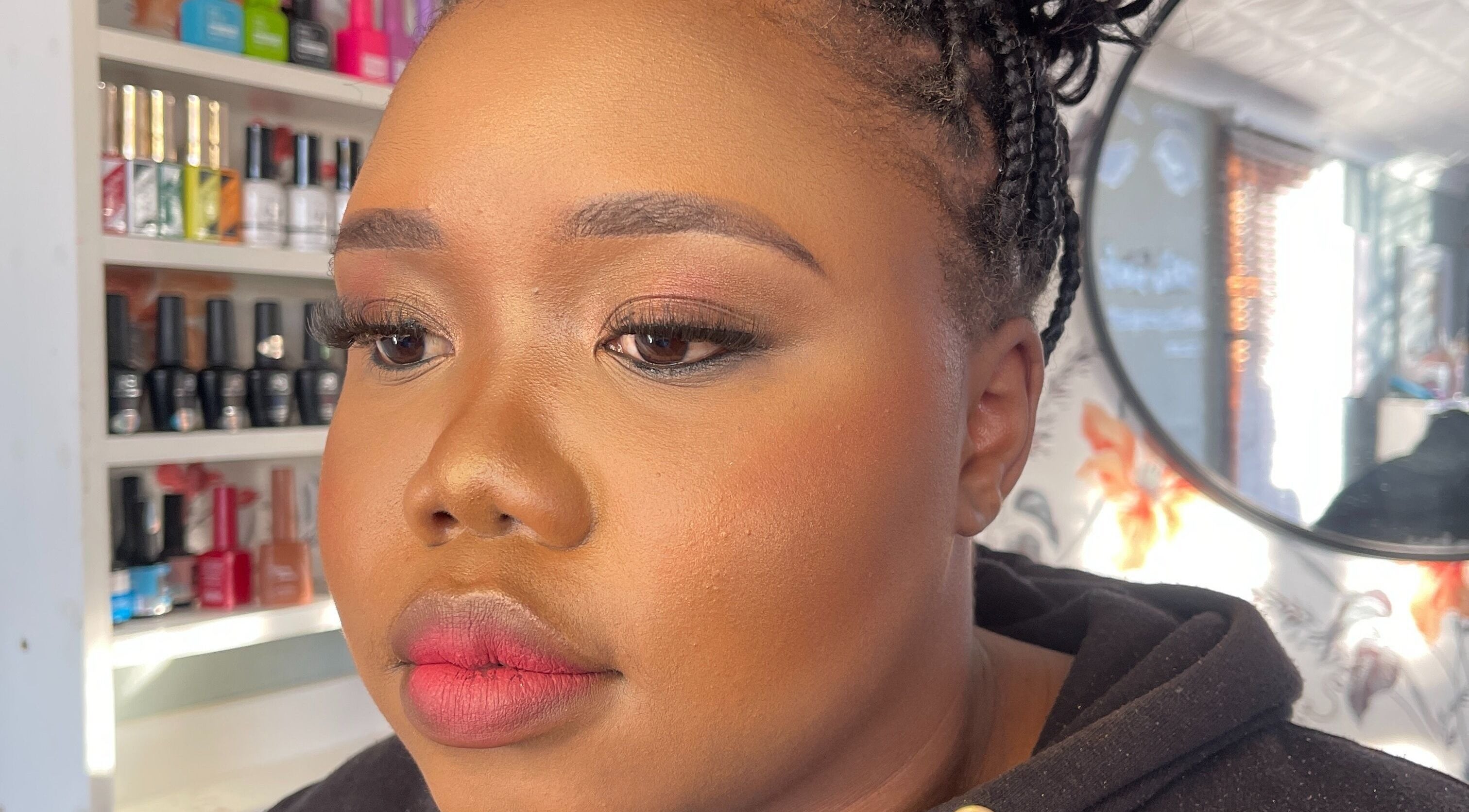 Close-up of a woman with makeup at African Girls Hair, Roodepoort, Gauteng, ZA. Shelves with nail polish are visible.
