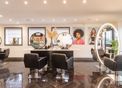 Modern salon interior at Maria Charles Hair Crawley, featuring stylish black chairs and lit mirrors in Crawley, England, GB.