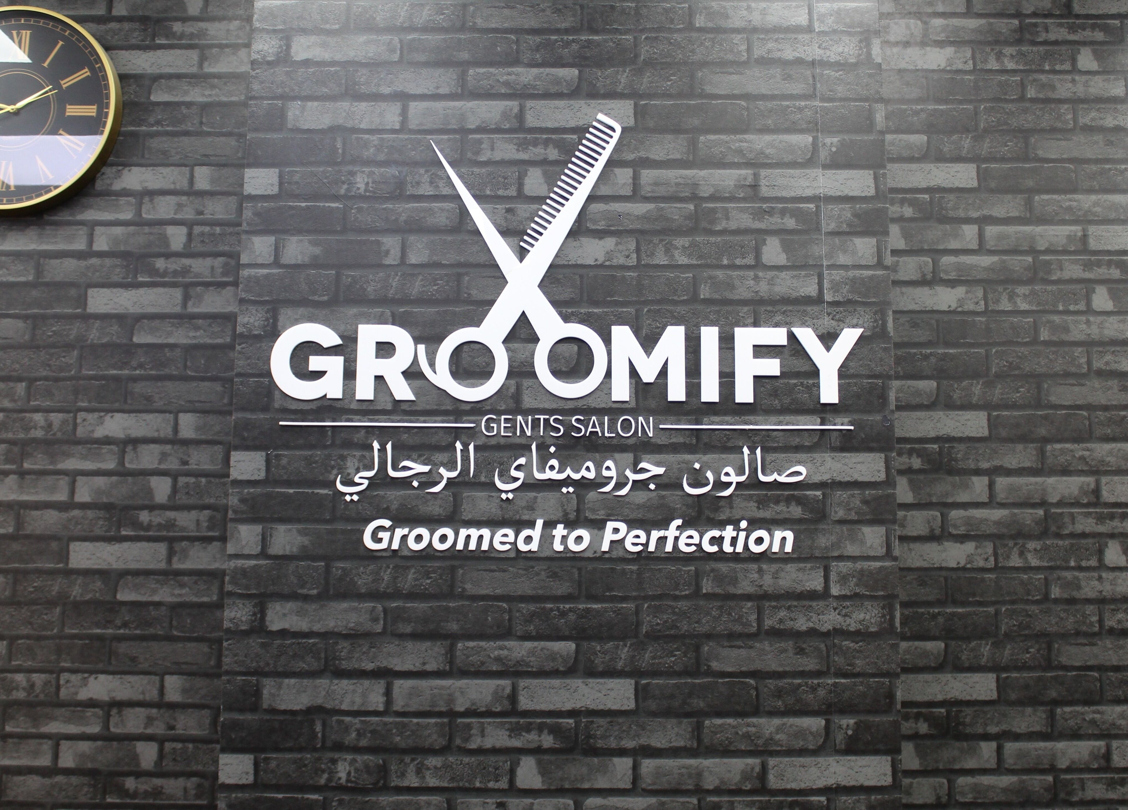 Brick wall with Groomify Gents Salon logo and clock in Abu Dhabi, AE.