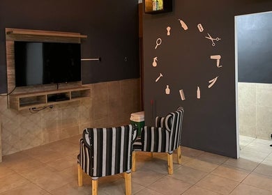 Sala de espera moderna en Like Barbería, San Juan, AR, con sillas rayadas y televisión en la pared.
