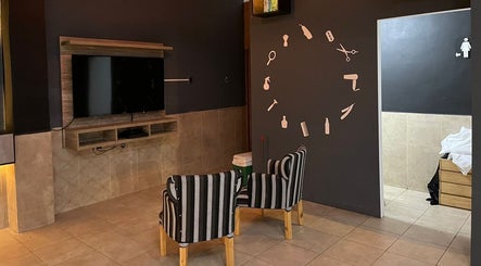 Sala de espera moderna en Like Barbería, San Juan, AR, con sillas rayadas y televisión en la pared.