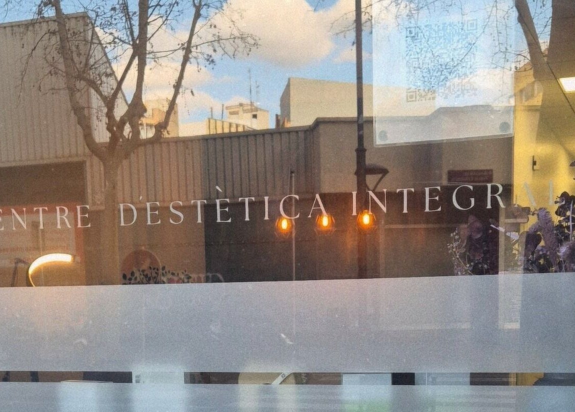 Entrada de GEO'S | Estética Integral en Reus, Catalunya, ES con reflejos de luces y flores en el vidrio