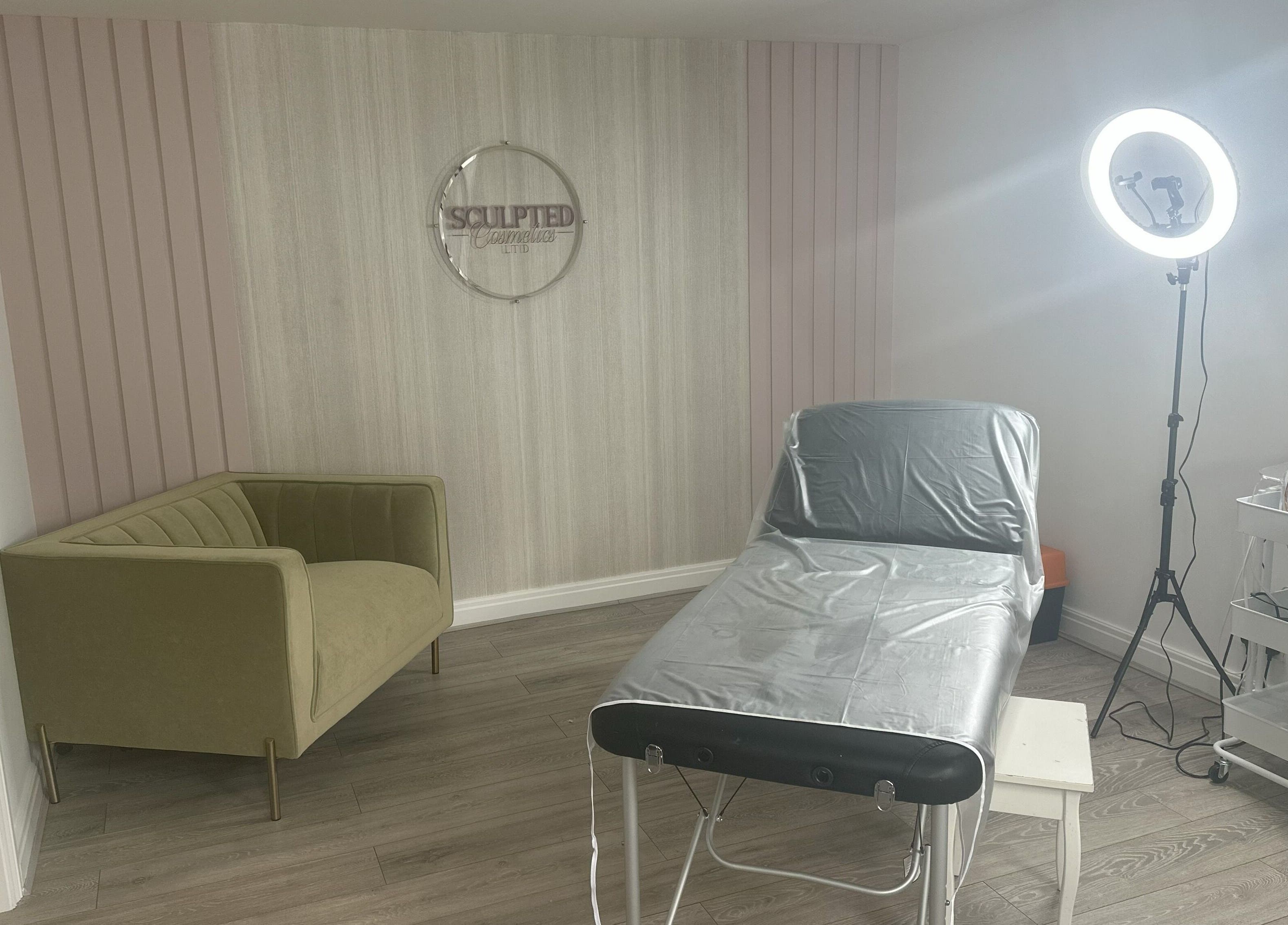 Treatment room at Sculpted Cosmetics Ltd, Orpington, England, GB featuring a stylish couch and therapy bed.