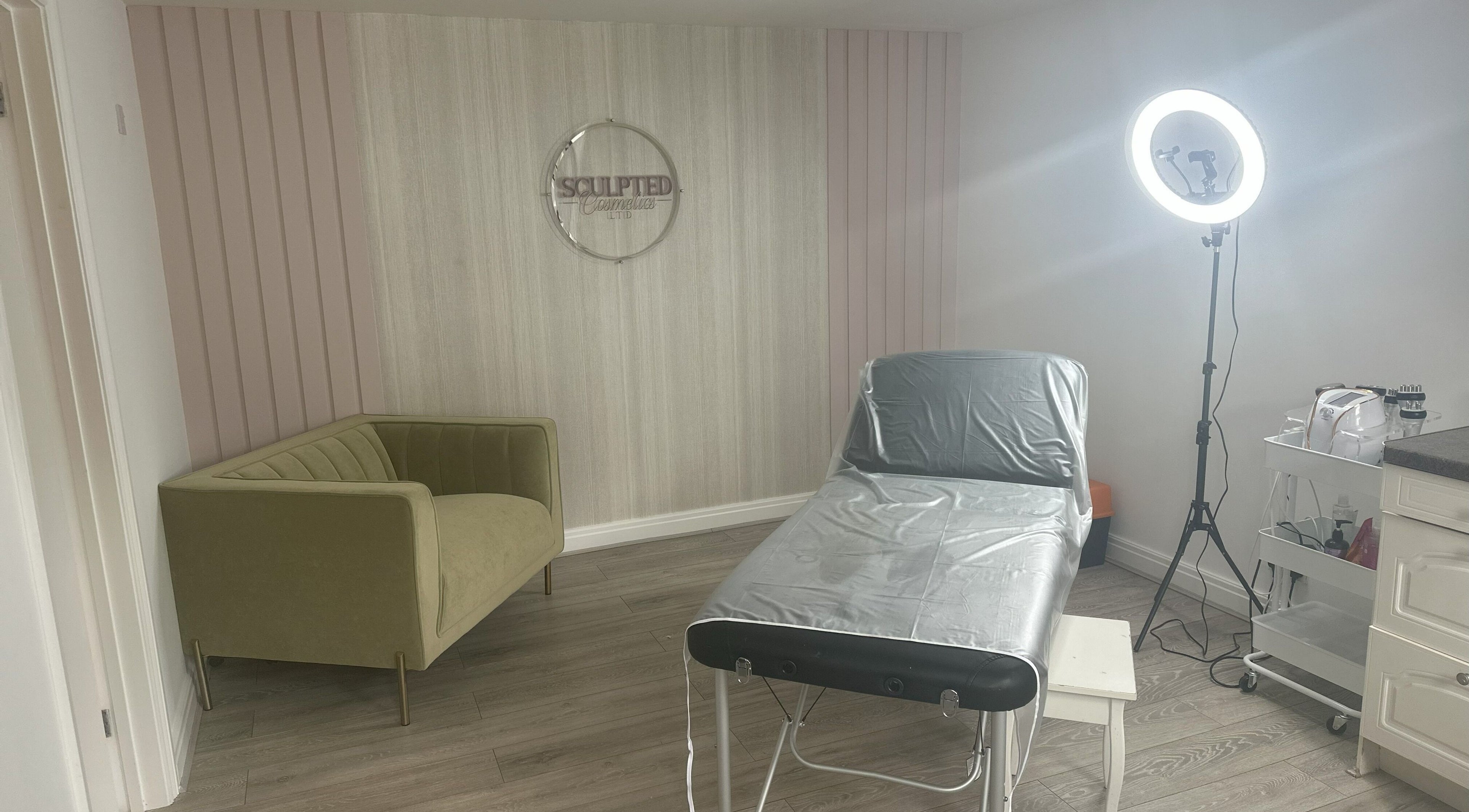 Treatment room at Sculpted Cosmetics Ltd, Orpington, England, GB featuring a stylish couch and therapy bed.