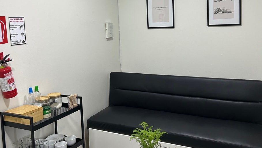 Sala de espera moderna en Podovita, La Reina, Región Metropolitana, CL, con sofá negro y decoración minimalista.