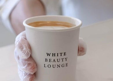 A gloved hand holds a coffee cup at Izghawa Branch, الريان, الريان, QA, featuring White Beauty Lounge branding.