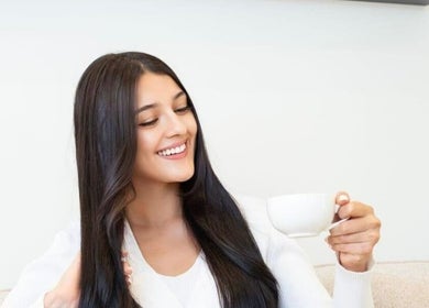 Smiling woman enjoys tea at Al-Kheesa Branch, Doha, Al Daayen, QA, embodying relaxation.