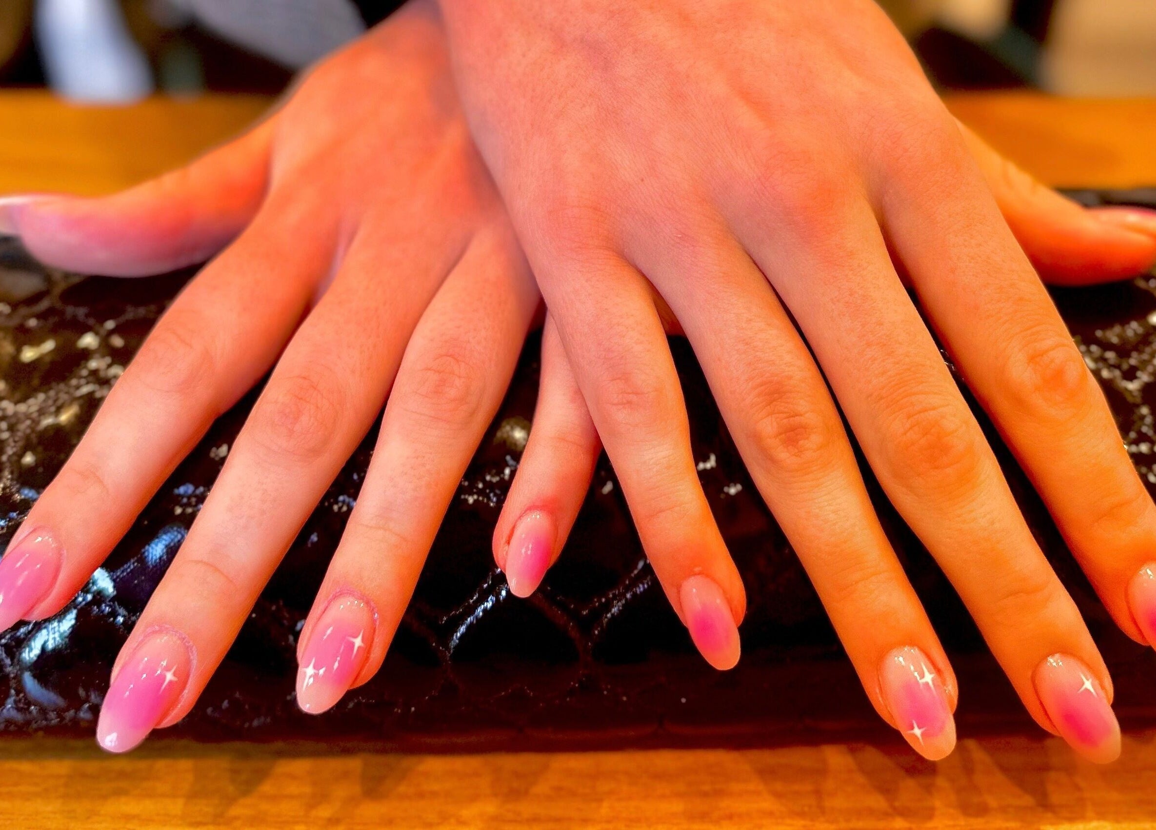 Manicured hands at Studio Rae, Aberdeen, Scotland, GB, showcasing pink ombre nails on a quilted clutch.