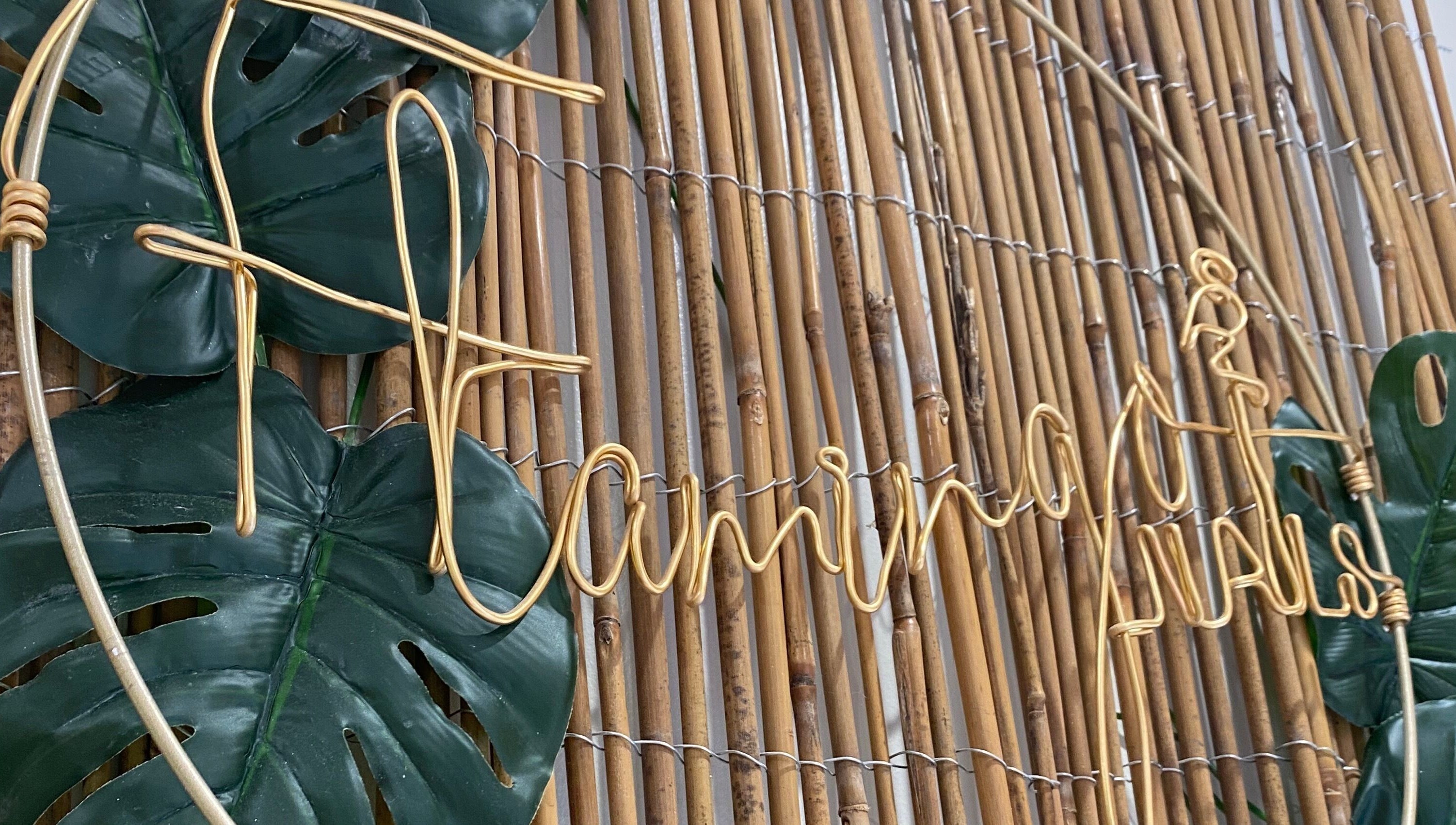 Flamingo Nails logo in golden wire on a bamboo wall at Park Gate, England, GB with lush green leaves.
