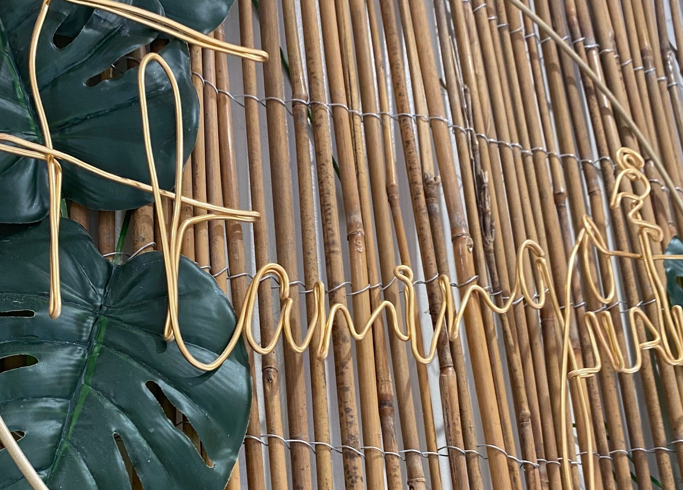 Flamingo Nails logo in golden wire on a bamboo wall at Park Gate, England, GB with lush green leaves.
