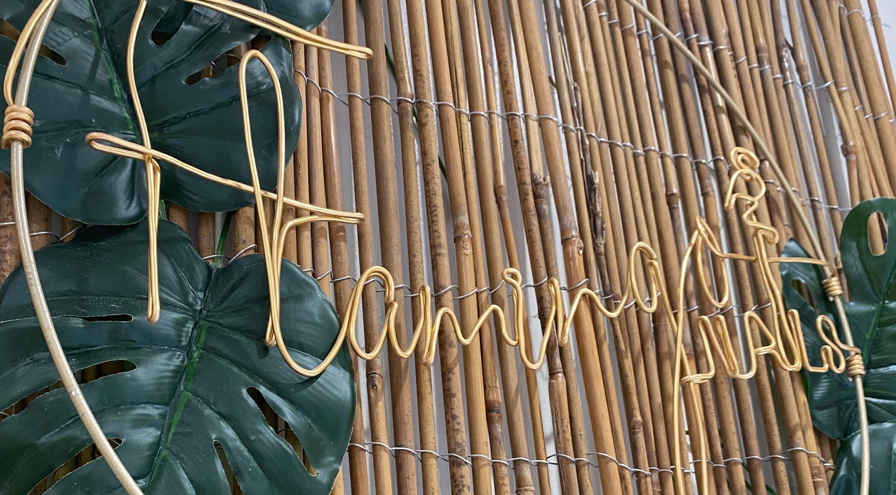 Flamingo Nails logo in golden wire on a bamboo wall at Park Gate, England, GB with lush green leaves.