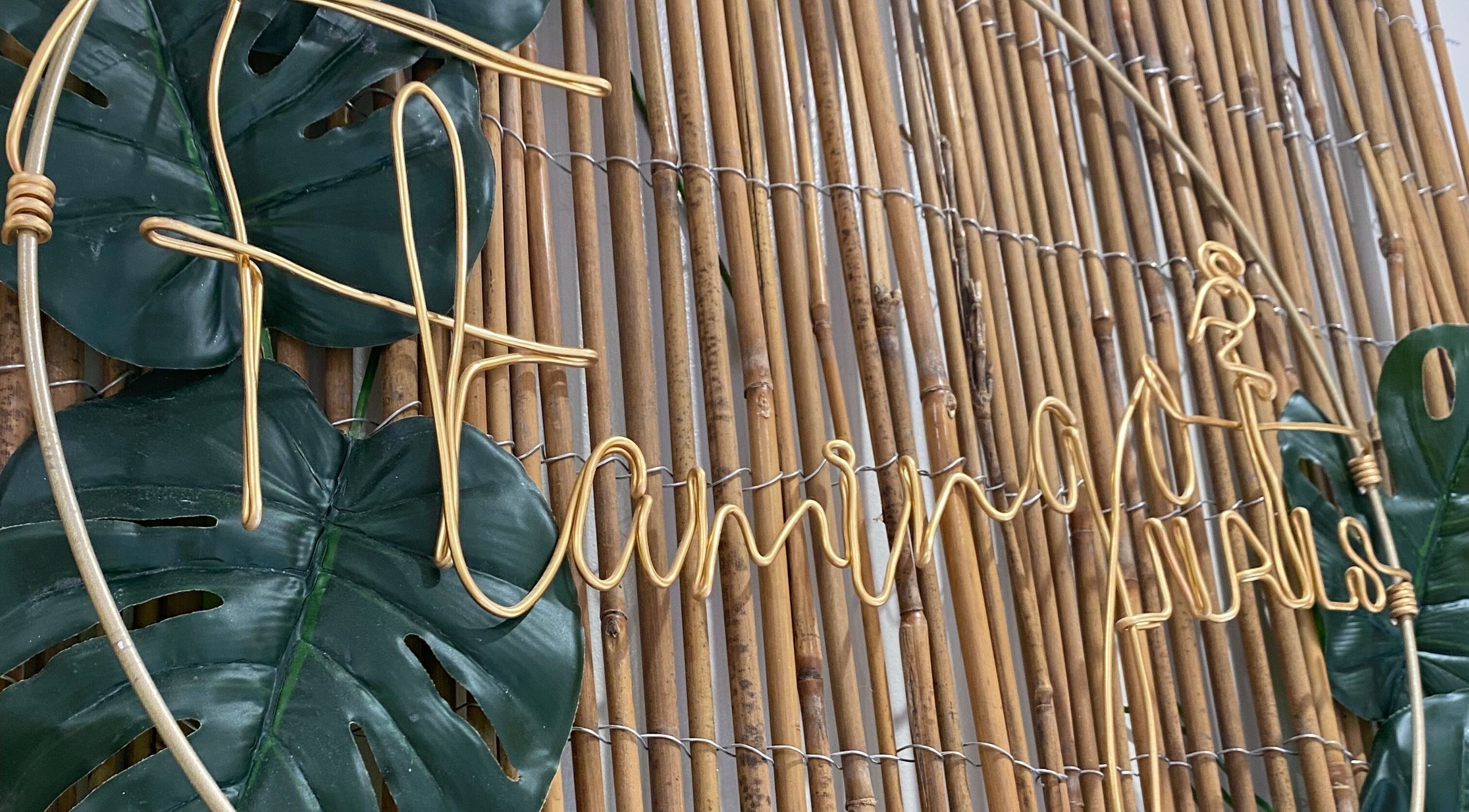 Flamingo Nails logo in golden wire on a bamboo wall at Park Gate, England, GB with lush green leaves.