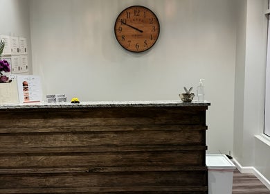Reception area at Gunston Massage with a wooden counter, clock, and vibrant flowers in Lorton, Virginia, US.