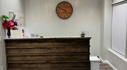 Reception area at Gunston Massage with a wooden counter, clock, and vibrant flowers in Lorton, Virginia, US.