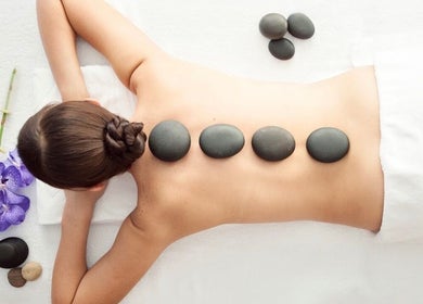 A relaxing hot stone massage at Gunston Massage, Lorton, Virginia, US with purple orchids nearby.