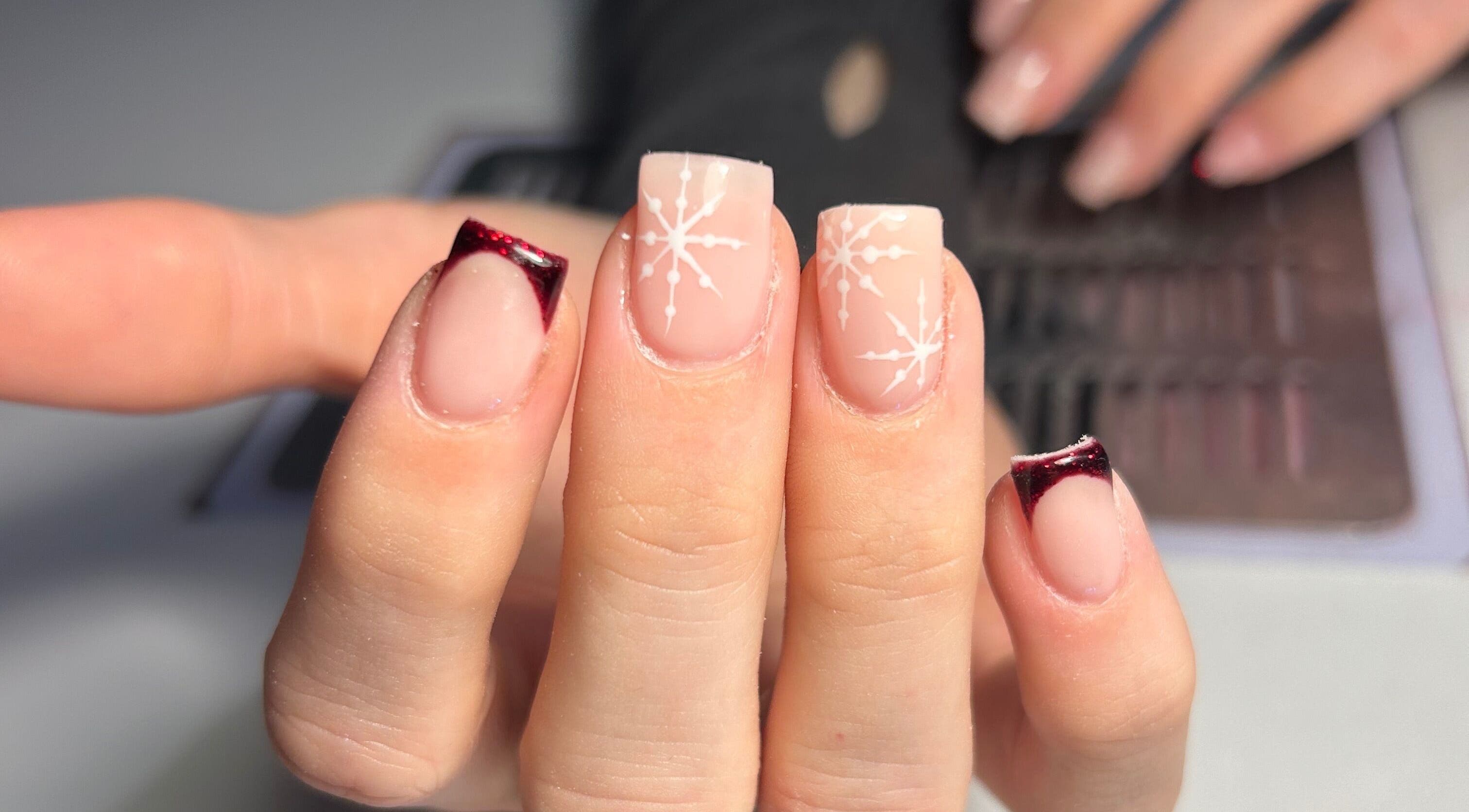 Intricate nail art at The Beauty Q in Feering, England, GB, showcasing snowflake designs with red tips.