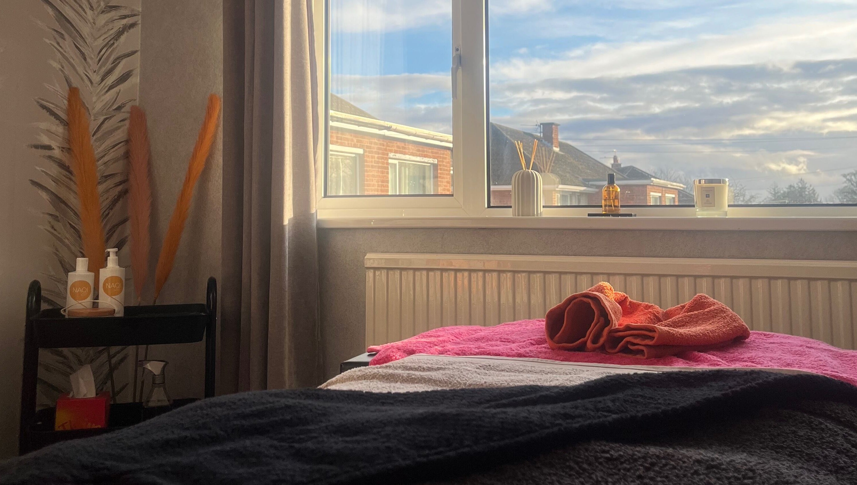 Cozy treatment room at The Body Club, Lisburn with window view, soothing decor, and folded towels.