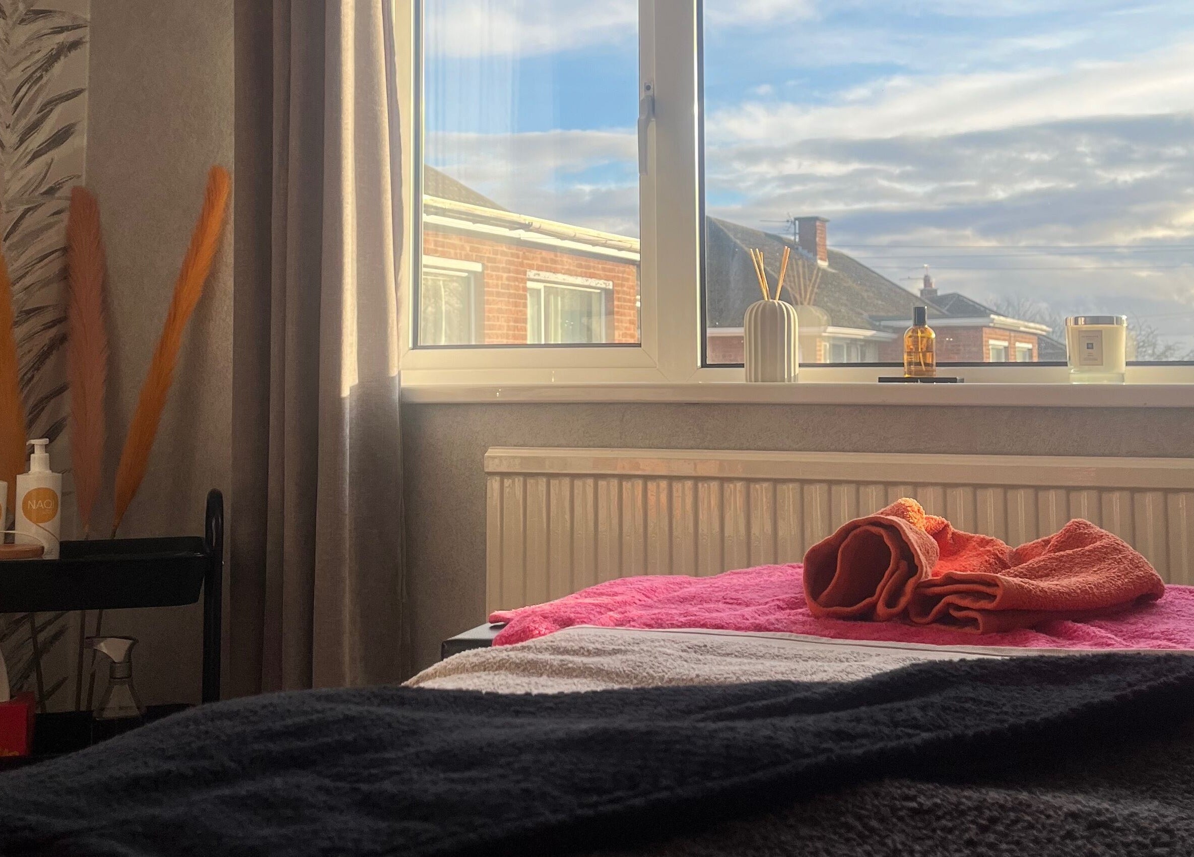 Cozy treatment room at The Body Club, Lisburn with window view, soothing decor, and folded towels.