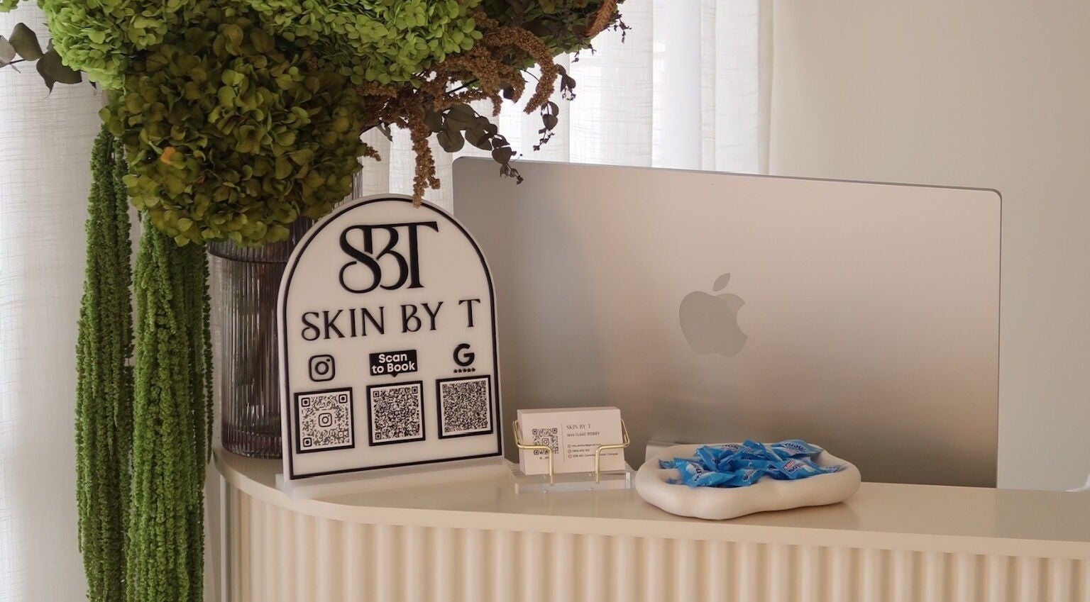 Skin By T reception desk in Campsie, New South Wales, AU, featuring a computer and decorative greenery.