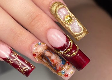 Nail art en tonos dorados y rojos en Nailsbycaprii, Avilés, ES. Diseño elegante y detallado.